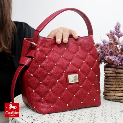 Mala de mão vermelha matelassê com rebites dourados e alça única em mesa branca com flores secas