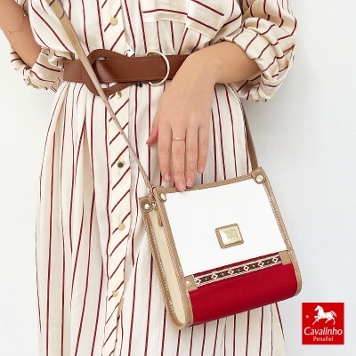 Bolsa Cavalinho branca, vermelha e bege com padrão étnico e placa metalizada, usada com camisa riscada e cinto castanho