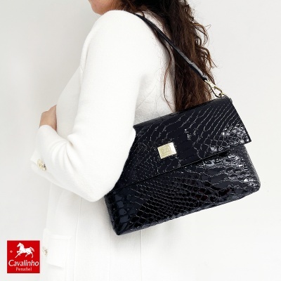 Mala preta com textura de pele de crocodilo e fecho dourado, usada ao ombro
