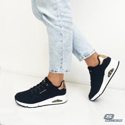 Ténis Skechers pretos com detalhes dourados e sola branca usados com jeans claros