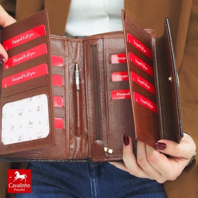 Carteira de couro castanha aberta com vários compartimentos para cartões e zíper, segurada por mãos.