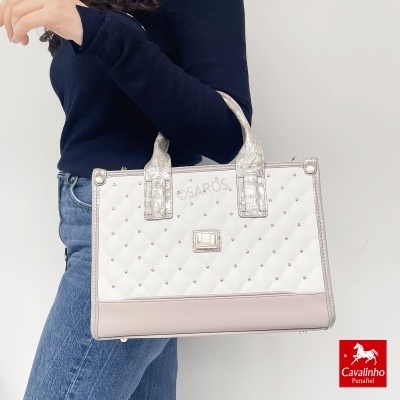 Mala quadrada acolchoada branca com detalhes prateados e alças prateadas sendo segurada por uma pessoa