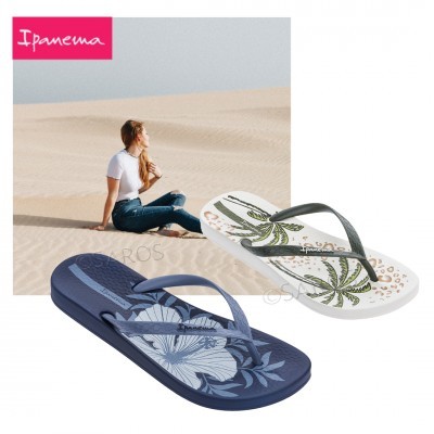 Dois chinelos Ipanema com padrões florais e folhas em primeiro plano e mulher sentada na areia ao fundo