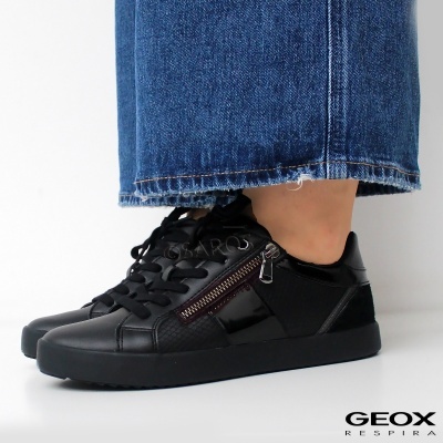 Ténis pretos em pele com fecho corredor e atacadores usados com calças de ganga azuis