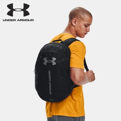 Mochila preta Under Armour com logótipo cinzento, usada por homem com camiseta amarela e calças cinza