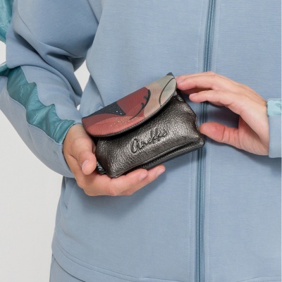 Carteira pequena preta com aba estampada, com bordado Anekke, segurada por pessoa com casaco azul claro.