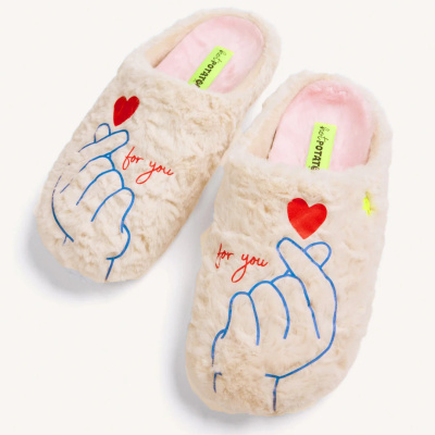 Chinelos peludos beige com estampa de mãos e corações vermelhos, interior rosa e etiqueta amarela