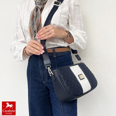 Mala Cavalinho em pele preta com faixa branca e alça preta larga usada com camisa branca bordada e jeans azuis