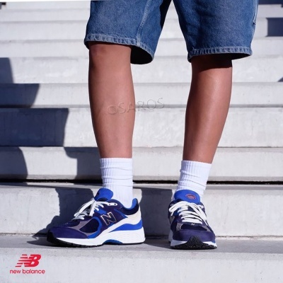 Sapatilhas New Balance azuis e brancas usadas por pessoa com calções de ganga e meias brancas em escadaria de cimento.