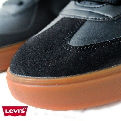 Detalhe do sapato preto com sola castanha e logo Levi's vermelho de fundo
