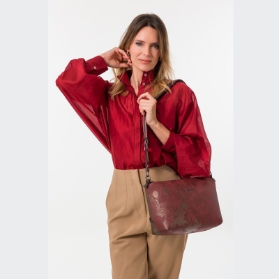 Mulher com camisa vermelha, calças bege e mala vermelha com padrão em relevo