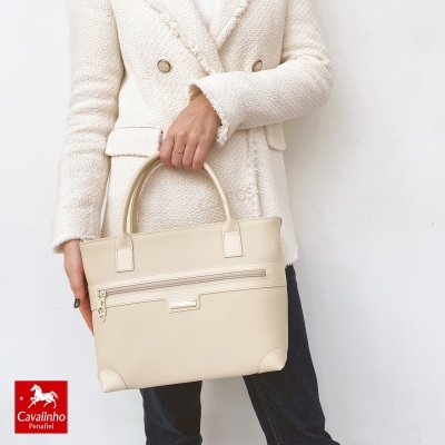 Mulher a segurar mala bege claro com casaco branco texturizado