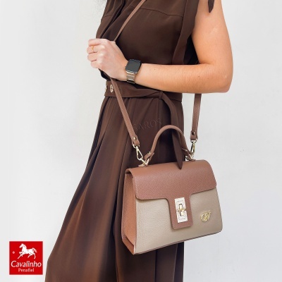 Mala de senhora em pele castanha e bege com fecho dourado e logótipo CV, usada com vestido castanho.