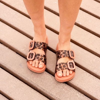 Sandálias com padrão animal print e fivelas castanhas usadas em chão de madeira