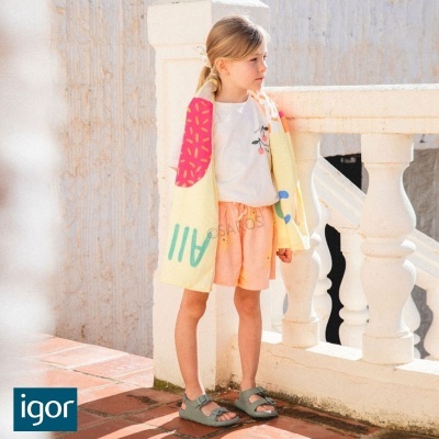 Criança com mochila colorida e roupa casual perto de grade branca ao ar livre