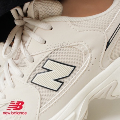 Ténis creme New Balance com textura de malha e couro sintético, logo N em relevo.