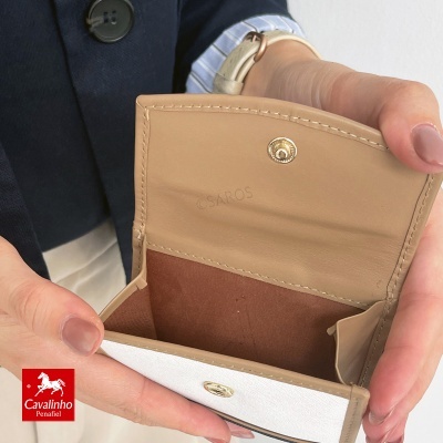 Carteira pequena aberta de pele bege e castanha sendo segurada por mãos femininas