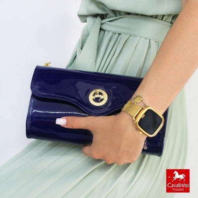 Carteira azul verniz com fecho dourado, mão feminina a segurá-la, fundo branco e logotipo Cavalinho