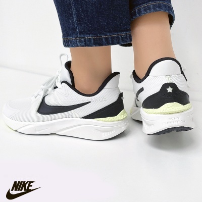 Ténis Nike brancos com detalhes preto e amarelo claro, usados com calças de ganga.
