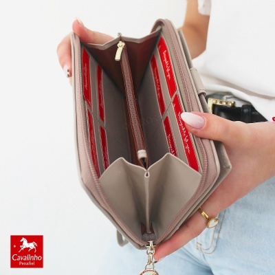Carteira bege aberta com compartimentos vermelhos e fecho dourado, segurada por uma pessoa