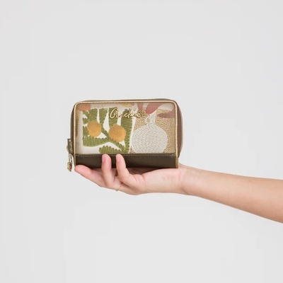 Carteira de mão em padrão vegetal com fecho, texto Anekke e detalhes texturizados.