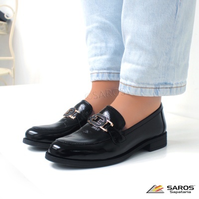 Sapatos pretos em couro brilhante com detalhe metálico, com calças de ganga claras