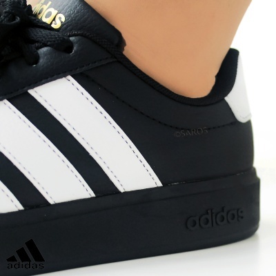 Sapatilha preta Adidas com riscas brancas e logótipo dourado