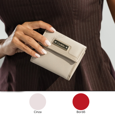 Carteira cinza pequena texturizada com placa metálica dourada e brilhantes segura por mão feminina