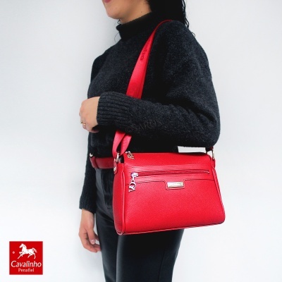 Mulher com mala de ombro vermelha e roupa preta diante de fundo branco