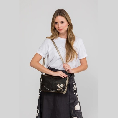 Mulher com t-shirt branca e saia preta segurando mala preta com detalhes dourados e corrente prateada