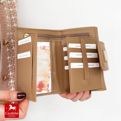 Carteira bege em pele aberta com compartimentos e etiquetas em branco com texto, segurada por mãos femininas