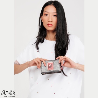 Carteira cinza com etiqueta rosa segurada por mulher de camiseta branca