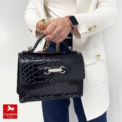 Mala preta padrão crocodilo com fecho dourado e corrente, pessoa com blazer branco e jeans azuis