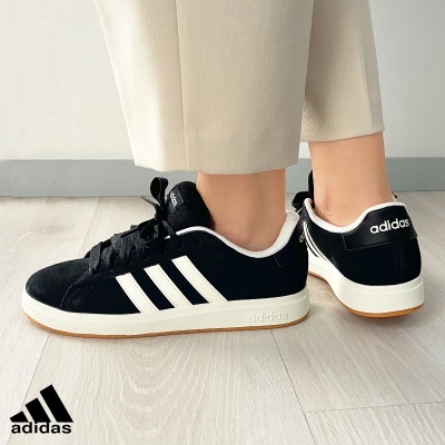 Ténis Adidas pretos com riscas brancas num chão claro