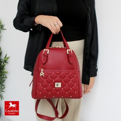 Mochila vermelha matelassê com tachas douradas e pendente, segurada por mulher