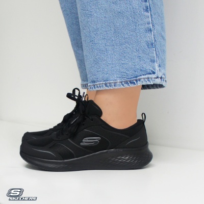 Ténis Skechers pretos com sola preta e logótipo S lateral, usados com calças jeans azuis