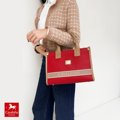 Mala de mão vermelha com detalhes bege e logo metal em mulher com casaco bege xadrez e calças jeans.