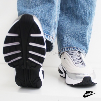 Ténis Nike branco e cinza com sola preta usados com calças de ganga