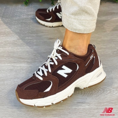 Ténis New Balance castanhos com sola branca e detalhes em branco.