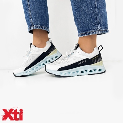 Sapatilhas desportivas brancas e pretas XTI com sola azul clara usadas com jeans azuis.