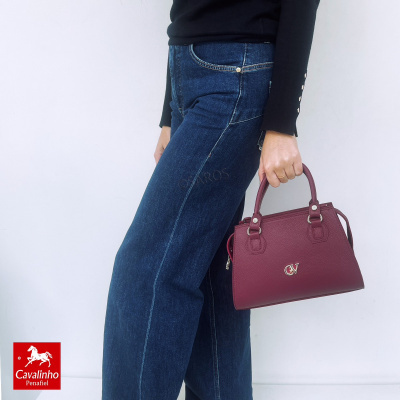 Pessoa com mala bordô em pele granulado e jeans azul escuro