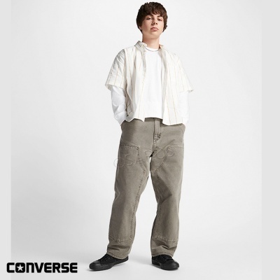 Homem com roupa casual clara e calças largas cinza com fundo branco e logo CONVERSE