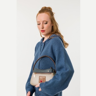 Mulher de cabelo ruivo com camisola azul segurando mala bege e verde escuro com patch de gato e coração vermelho