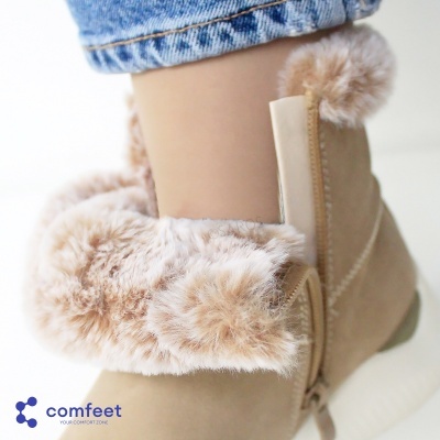 Bota bege com pelúcia e pompons, parte de jeans azul visível