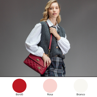 Bolsa de ombro bordô acolchoada com alça e detalhes dourados, usada por mulher com colete cinza, camisa branca e saia xadrez