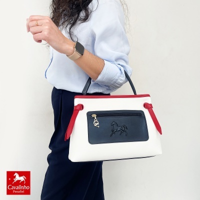 Mala bicolor branca, azul e vermelha com bolso frontal azul e pendente dourado em forma de cavalo e letra C