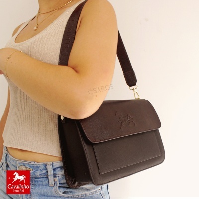 Bolsa de couro castanho escuro com padrão de cavalo e alça larga em couro, vista num modelo com top bege e calças de ganga azuis