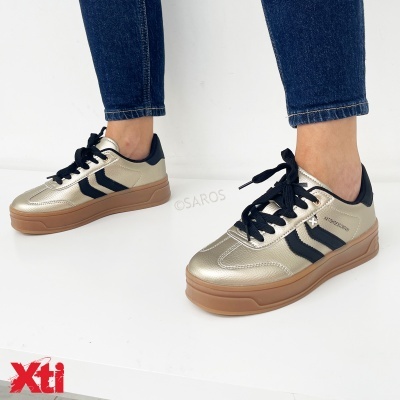 Ténis dourados com sola castanha e detalhes pretos, usados com jeans azuis.