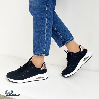 Ténis Skechers pretos com detalhes dourados e sola branca, usados com jeans azuis