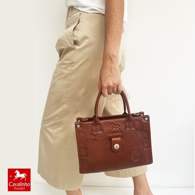 Bolsa castanha em pele com textura segurada por pessoa com saia bege clara e blusa branca